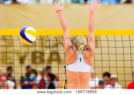 Volleyball player is a female beach volleyball player jumping up getting ready to block the ball.