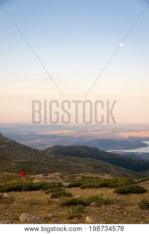 Girl climber contemplates from the top of the mountain a amazing sunset and the moonrise. Navacerrada Spain.