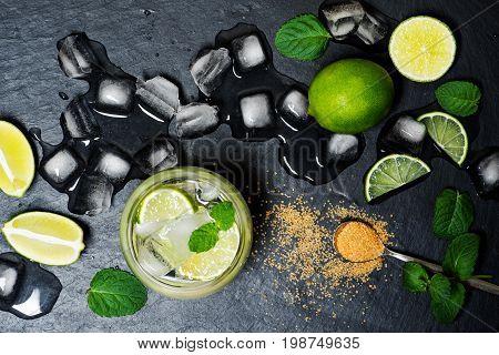Refreshing mint cocktail mojito with rum and lime, cold drink or beverage with ice on black background, top view