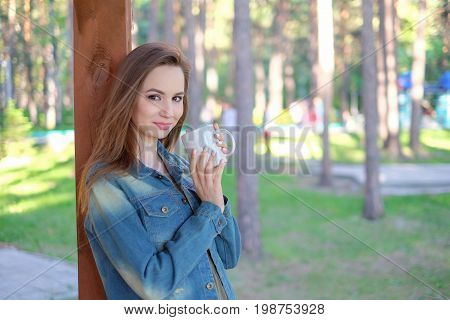 Close up portrait of a smiling young girl in hat holding take away coffee cup outdoors