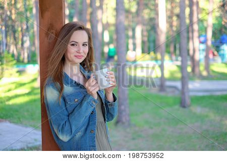 Close up portrait of a smiling young girl in hat holding take away coffee cup outdoors