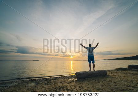 man on sand beach looking on sunrise with hands up
