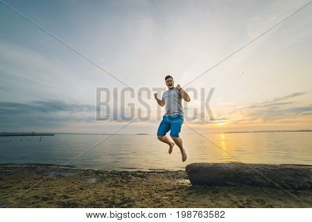 man jump on sand beach with sunrise on background