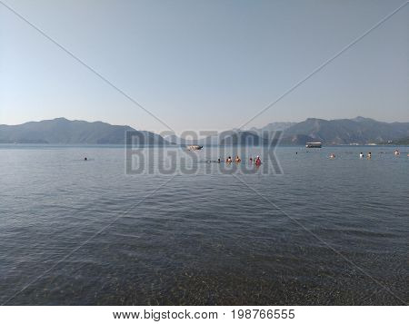 Beatiful sea summer panorama.  Beach scene at Pukka region, yachts, boats, mountains, shot at Marmaris, Turkey. blue sky, tourists in swimsuits, umbrellas, people resting, swimming
