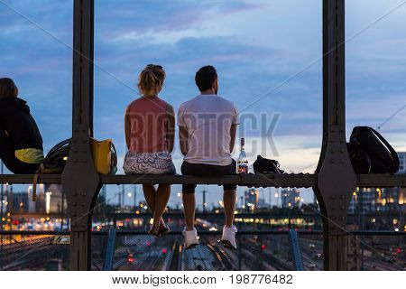 Young couple in love on romantic date sitting on railway bridge with a bottle of wine and watching the sunset over Munich urban city center. Just the two of us.
