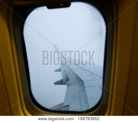 Looking trough window of an aircraft plane wing in fog. View from plane window during landing or takeoff in extreme foggy weather. Flying through clouds.
