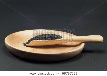 Black sesame in a wooden spoon against a black background.
