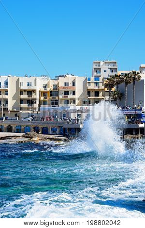 BUGIBBA, MALTA - MARCH 28, 2017 - Sea crashing onto the rocky coastline with a shopping street to the rear Bugibba Malta Europe, March 28, 2017.