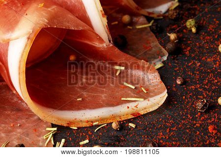 A close-up picture of tasty twisted prosciutto slices on a black background. Beautiul salty ham and red spices. Delicious pink appetizers for beer. Restaurant food.