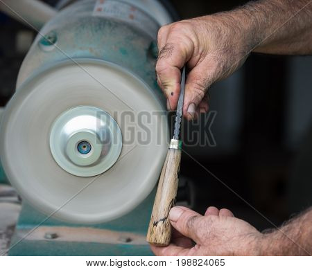 The hands of the craftsman carefully holds a custom made knife against the buffing wheel to carefully polish the finish of the handle.