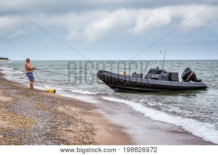 Man pulling a rope to keep his boat on shore.
Gotska sandon Sweden - August 2 2017: Side view of a caucasian man on an island beach in the Baltic sea pulling a rope to stop his black speed boat from drifting away.