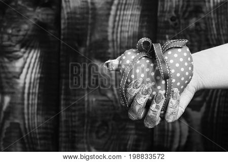 female hand smeared in golden paint or glister holding handmade pink polka dots selective focus valentine heart on brown vintage studio background copy space