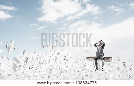 Young shocked businessman sitting on book and covering eyes with palms