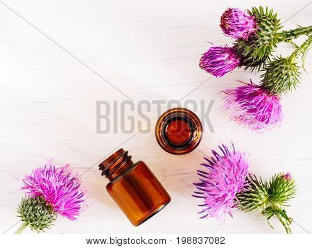 burdock oil in small glass bottle and burdock flowers on white wooden table. Top view or flat lay. Copy space.
