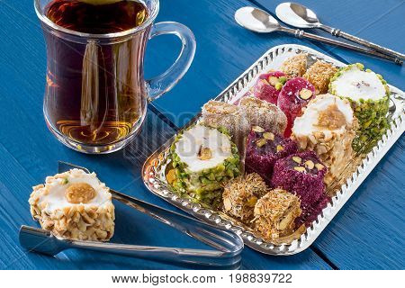 Eastern sweets. Assorted traditional Turkish delight (Rahat lokum) on blue wooden background. Turkish delight with different nuts and coconut shavings tea in glass (armud) tongs for sweets spoons