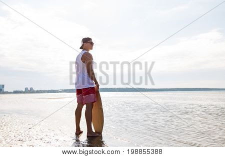 skimboarding, water sport and people concept - happy smiling young man with skimboard on summer beach