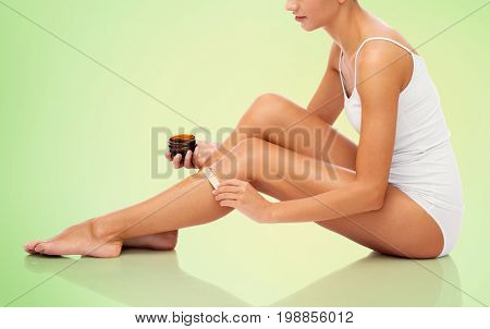 beauty, depilation, epilation, hair removal and people concept - beautiful woman with applicator applying depilatory wax to her leg over green background