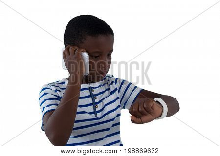 Boy looking at his smart watch while talking on mobile phone against white background