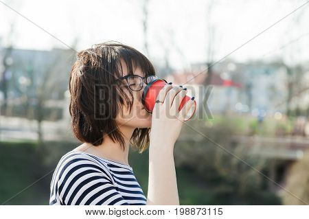 A girl in a striped T-shirt is drinking coffee with a blurred background
