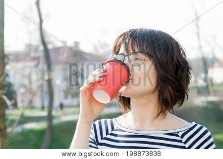 A girl in a striped T-shirt is drinking coffee with a blurred background
