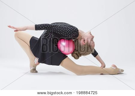 Sport Concepts. Caucasian Female Rhythmic Gymnast In Professional Competitive Black Sparkling Suit Doing Backbend Stretching Exercise With Ball in Studio On White. Horizontal Image