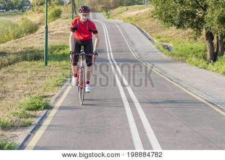 Cycling Ideas. Portrait of Professional Male Cyclist Doing Uphill on Road Bike. Fully Equipped in Professional Outfit. Horizontal Shot