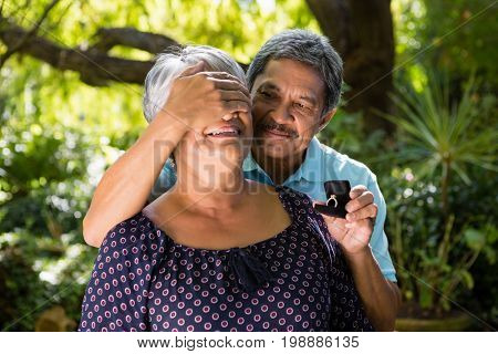 Senior man covering woman eyes while gifting her ring in garden