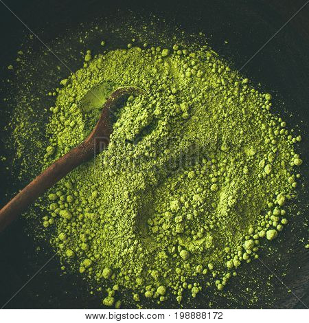 Japanese Matcha green tea powder in dark wooden bowl with spoon, top view, square crop. Clean eating, healthy, diet food concept