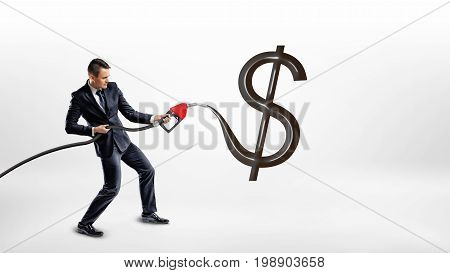 A businessman holds a gas pump nozzle and makes a huge black glossy USD sign on a white background. Oil and gas industry. Commodity exchange. Cost of energy sources.