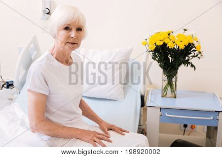 Recovering quickly. Charming but still pale elderly woman getting better and feeling well enough for sitting up in her bed