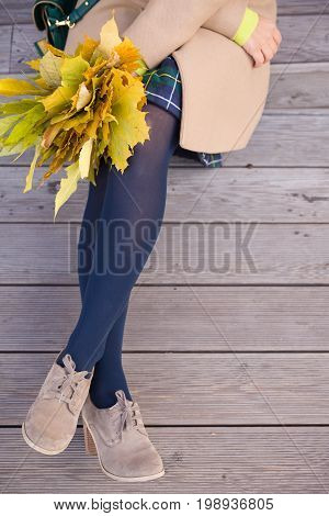 Top view on woman's hands holding beautiful bunch of yellow marple leaves. Young woman with bouquet of autumn leaves sitting on wooden bridge in park.autumn thanksgivining and lifestyle concept