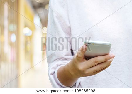 Woman hand using smart phone over blur store with bokeh background business and technology concept gen Z digital marketing lifestyle the internet of things social media network