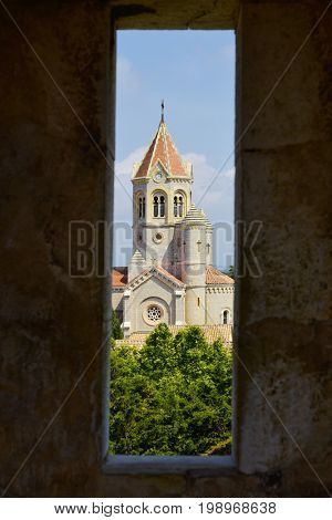 a view of the Lerins Abbey in the Saint-Honorat island, France, highlighting the lantern tower of its church, seen through an embrasure of a stone wall