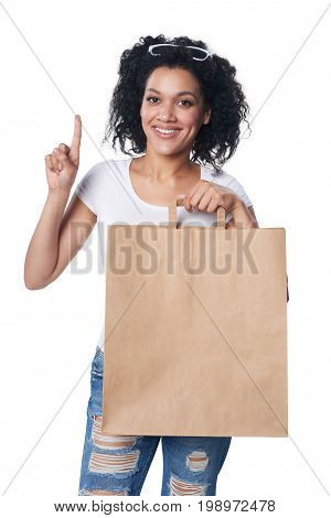 Happy mixed race woman holding craft shopping bag with blank copy space and showing directing one finger up