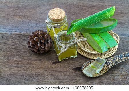 Fresh aloe vera gel on wooden spoon with aloe vera essential oil and pine on wooden table