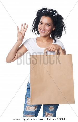 Happy mixed race woman holding craft shopping bag with blank copy space and showing four fingers