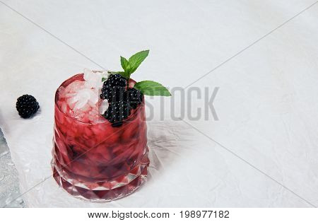 Summer coctail with ice cubes, fresh green mint and sappy blackberries in a pink glass on a white background, copy space, blackberry on a white table-cloth.