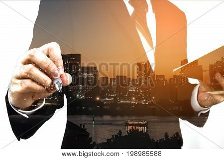 Businessman holding memo and ready to write down with big town or city in the background. Double exposure panoramic view contemporary megalopolis background orange sun light business concept