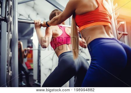 European girl in a gym with long hair is engaged with a personal trainer on the simulator bar for squatting. Concept training under the guidance of a mentor, group exercise in sports.