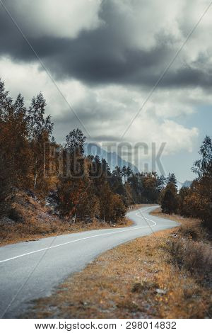 A Dull Moody Serpentine Road In Autumn Mountains Surrounded By Dry Native Grasses, Hills, Birches An