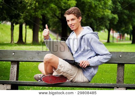 un adolescente con Ambientazione esterna portatile. seduto nel parco mobile internet