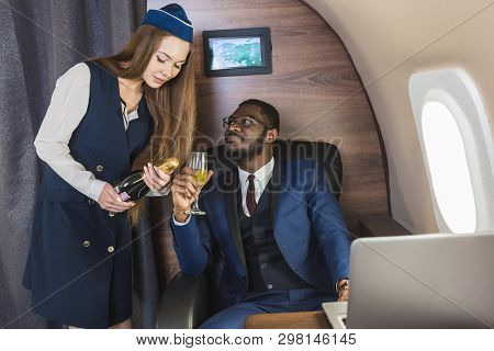 Young Successful Afro-american Businessman In Glasses And A Stewardess Shows A Bottle Of Wine In The
