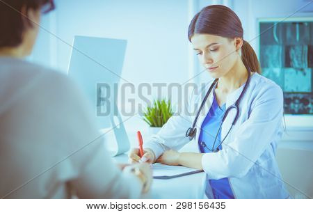 Doctor and patient discussing medical problems in a hospital consulting room. Doc filling in a patient's form