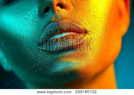 Fashion model woman skin face in bright sparkles, colorful neon lights, beautiful sexy girl lips, mouth. Trendy glowing gold skin make-up. Art design make up. Glitter metallic shine makeup