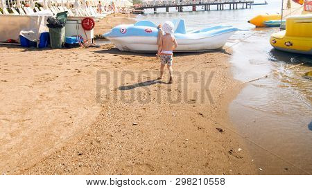 Rera View Image Of Little Toddler Boy Walking On Sea Beach Toward Boats And Catamarans