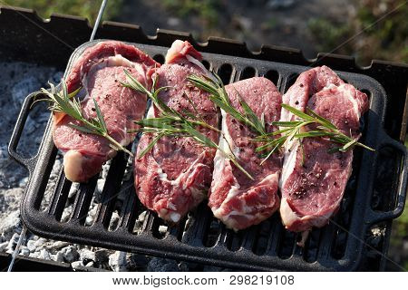 Cooking Outdoors. Raw Juicy Beef Steaks With Rosmary On Grill.