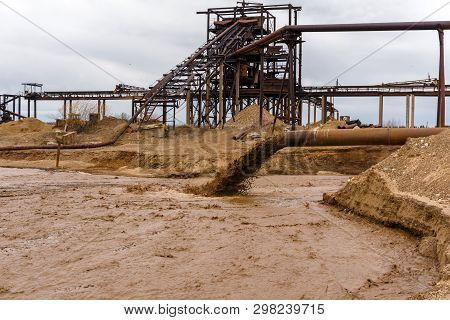 Rusty Pipe On The River Bank, From Which Sewage Flows, Dirty Sand Slurry, And Stationary Rusty Gravi