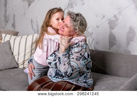 Grandmother And Her Little Granddaughter Are Watching Movies Together And Playing On The Device Whil