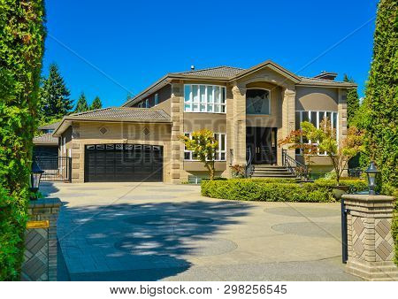 Front Yard Of Luxury Family House With Paved Driveway In Front On Blue Sky Background