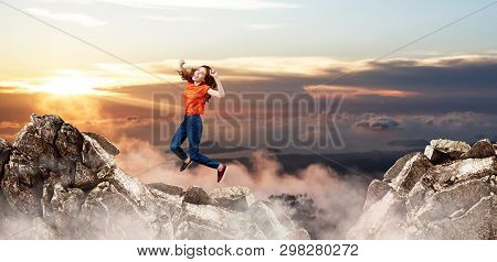 Redhead Woman Jumps Through The Gap Between Hills Over Cliff On Blue Sky Background.